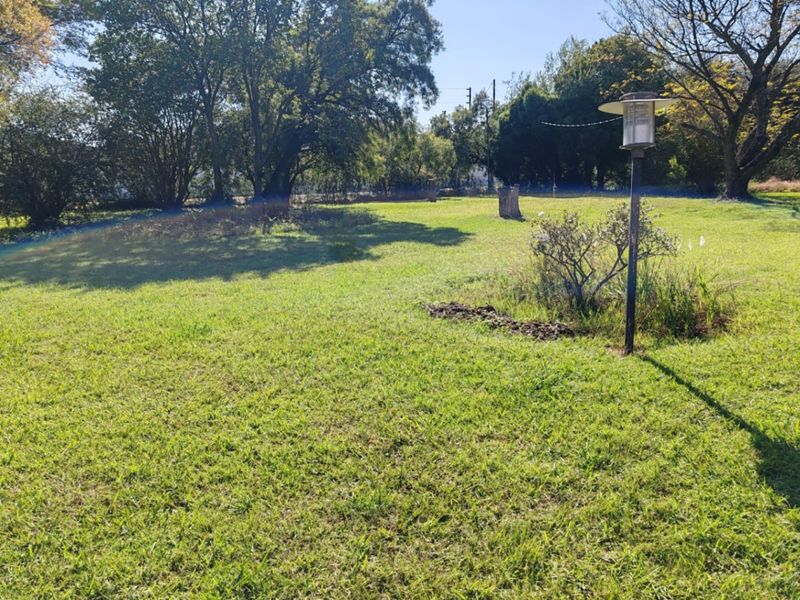 A spacious, well-maintained grassy garden area featuring mature trees and a fixed garden lamp post.