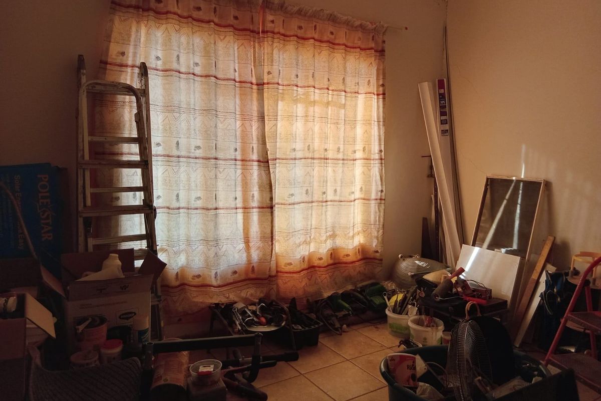 A cluttered room featuring tiled flooring and natural light through window curtains, currently used for storage and requiring maintenance and clearing.
