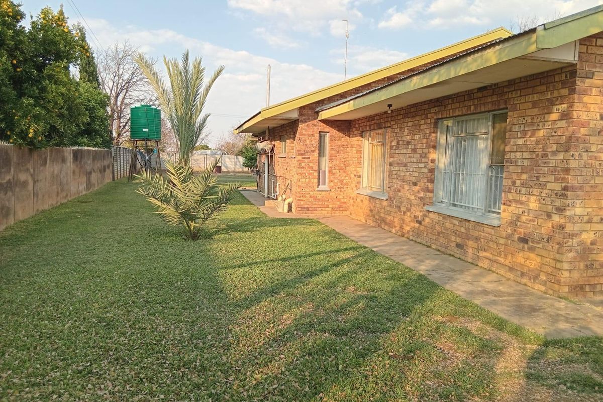 Rear view of the property featuring a face brick facade, corrugated metal roof, and a spacious garden with a water storage tank.