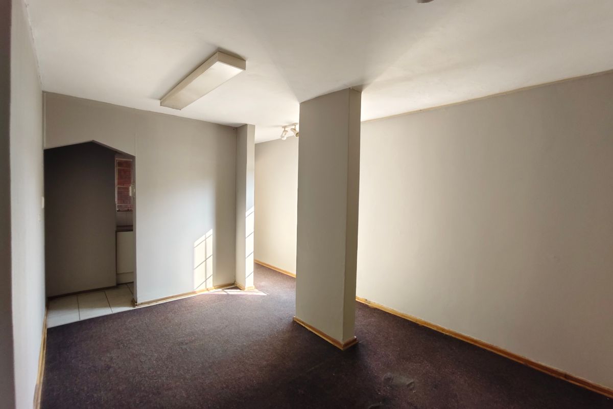 An empty, open-plan living area featuring neutral wall tones, carpeted flooring, and a central structural column, providing a blank canvas for renovation.
