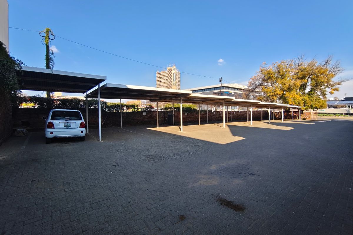 A paved commercial parking area featuring multiple covered parking bays and a secure brick boundary wall.
