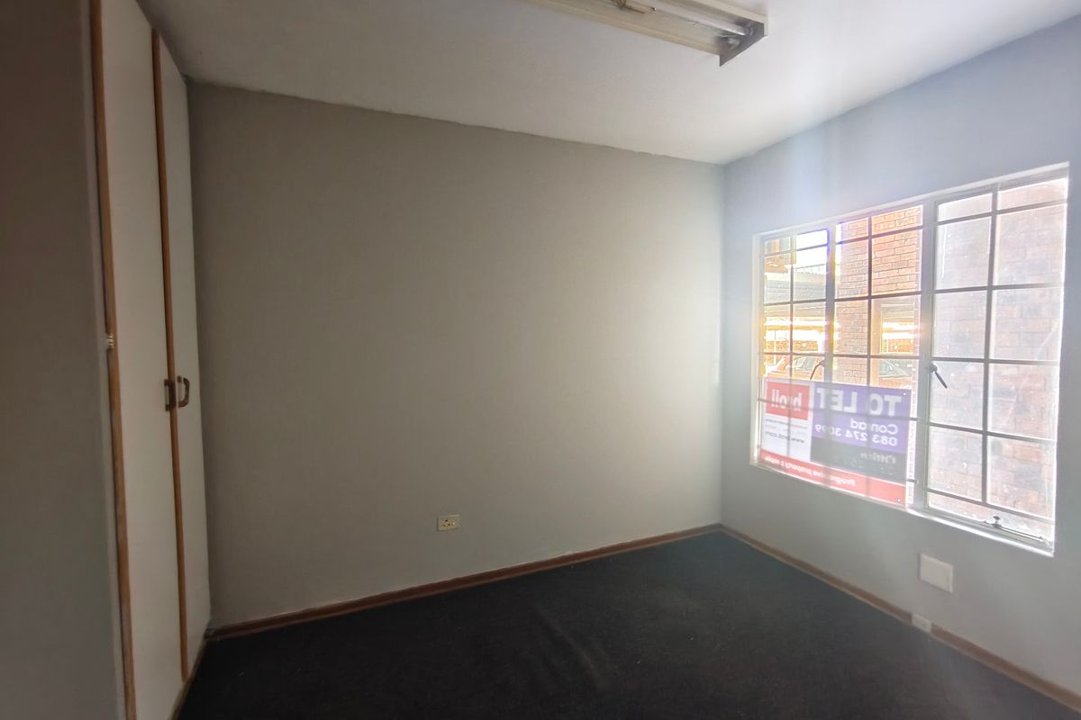 An empty bedroom featuring built-in cupboards, carpet flooring, and a window with security bars.