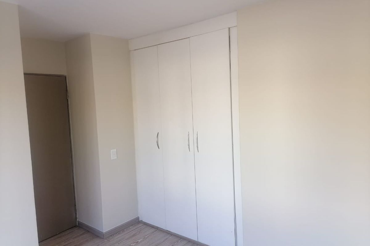 A clean, empty bedroom featuring neutral walls, laminate flooring, and a built-in wardrobe with white doors.