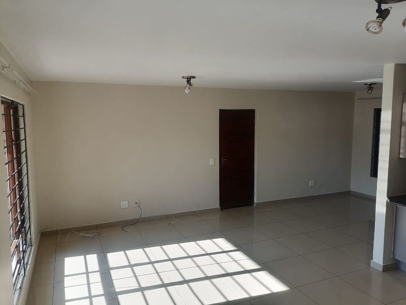 A spacious, empty open-plan living area featuring neutral tiled flooring, large windows with security bars, and a clean, minimalist aesthetic.