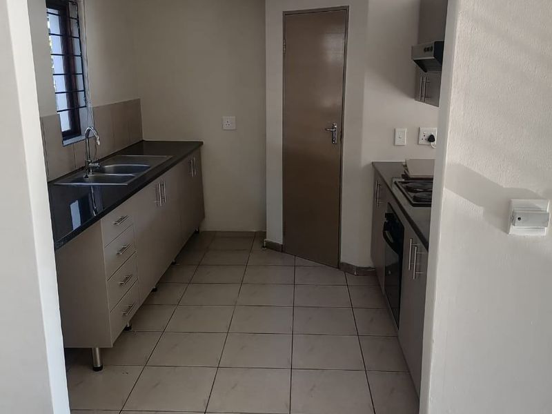 A clean, functional kitchen featuring built-in cabinetry, granite countertops, a double basin sink, and integrated cooking appliances with neutral tiled flooring.