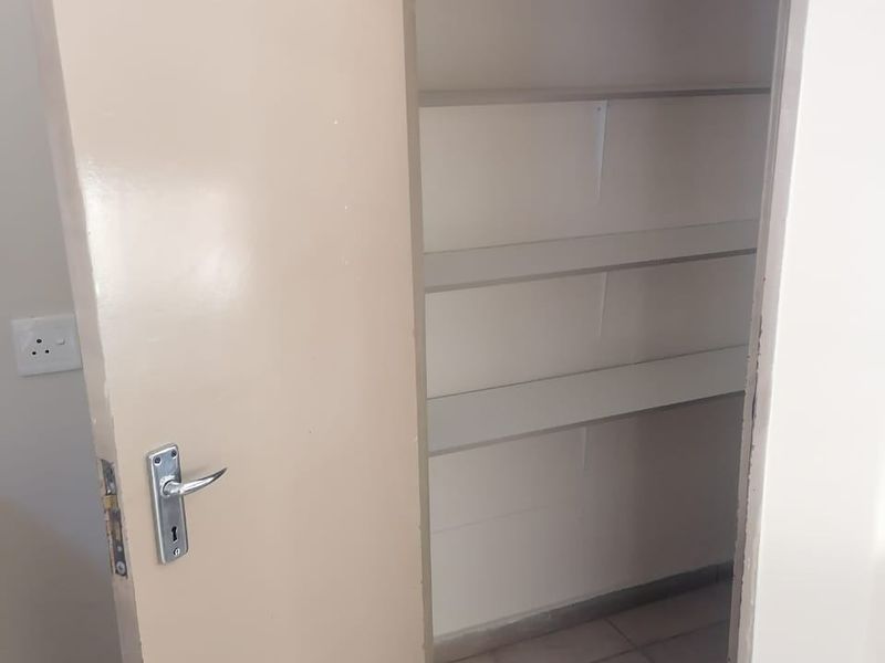 A functional walk-in pantry or storage cupboard featuring built-in shelving and tiled flooring.