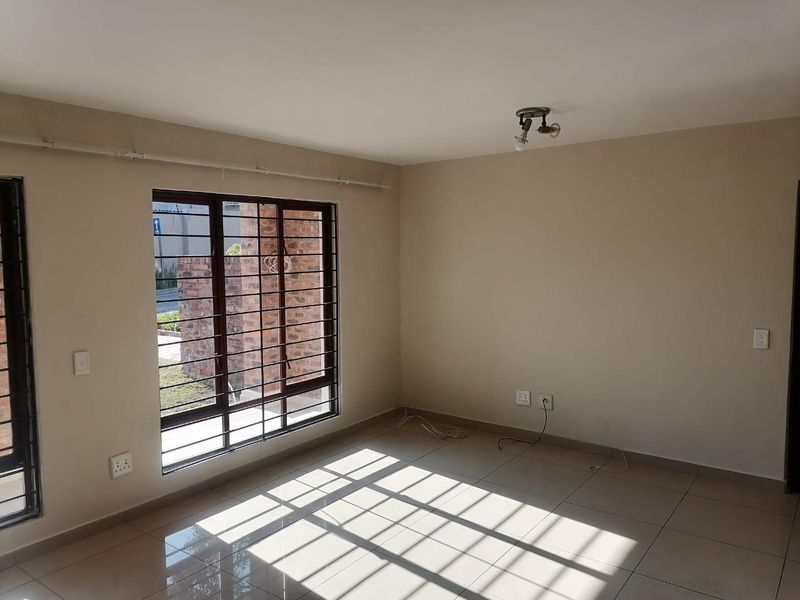 A bright, empty living room featuring neutral tiled flooring, large windows with security bars, and clean wall finishes.