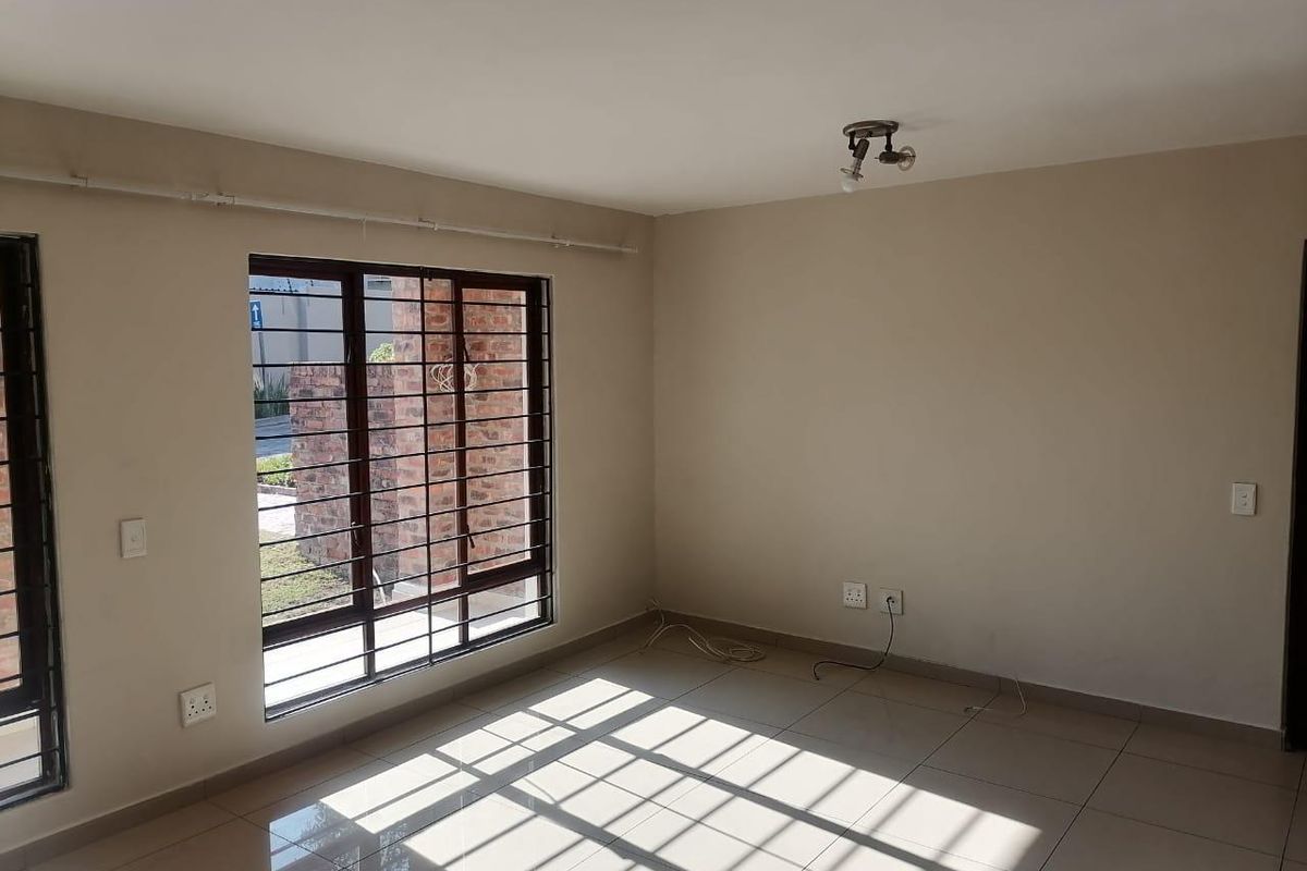 A bright, empty living room featuring neutral tiled flooring, large windows with security bars, and clean wall finishes.