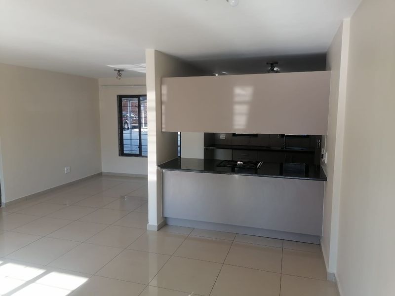 An open-plan living and kitchen area featuring modern cabinetry, granite countertops, a built-in hob, and neutral tiled flooring throughout.