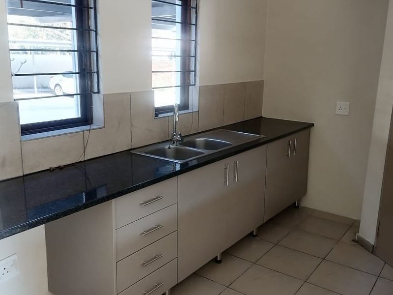 A clean, functional kitchen featuring granite countertops, double basin sink, tiled flooring, and ample built-in cabinetry with a neutral finish.