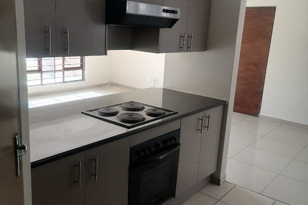 A clean, modern kitchen featuring neutral-toned built-in cabinetry, a fitted electric hob, oven, and extractor fan, with tiled flooring throughout.