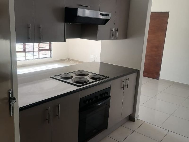 A clean, modern kitchen featuring neutral-toned built-in cabinetry, a fitted electric hob, oven, and extractor fan, with tiled flooring throughout.