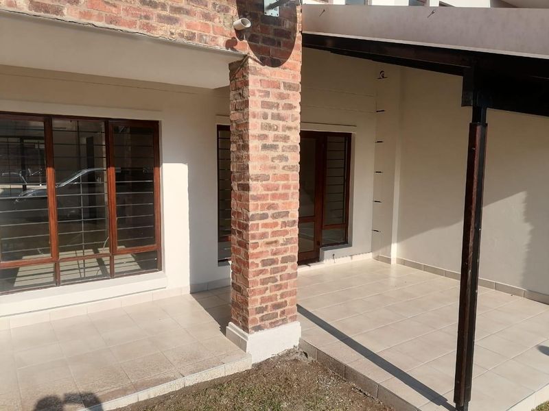 A covered patio area featuring tiled flooring, an exposed brick support pillar, and timber-framed windows with security bars.