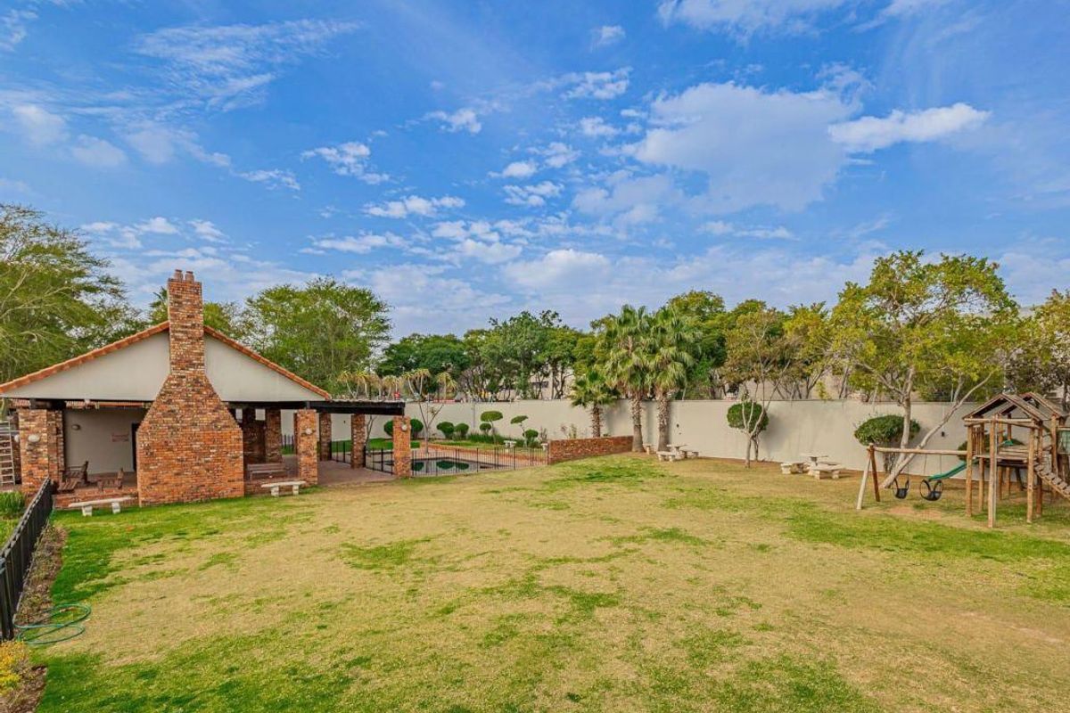 Spacious rear garden featuring a large lawn, a covered brick patio with a fireplace, and a swimming pool area.