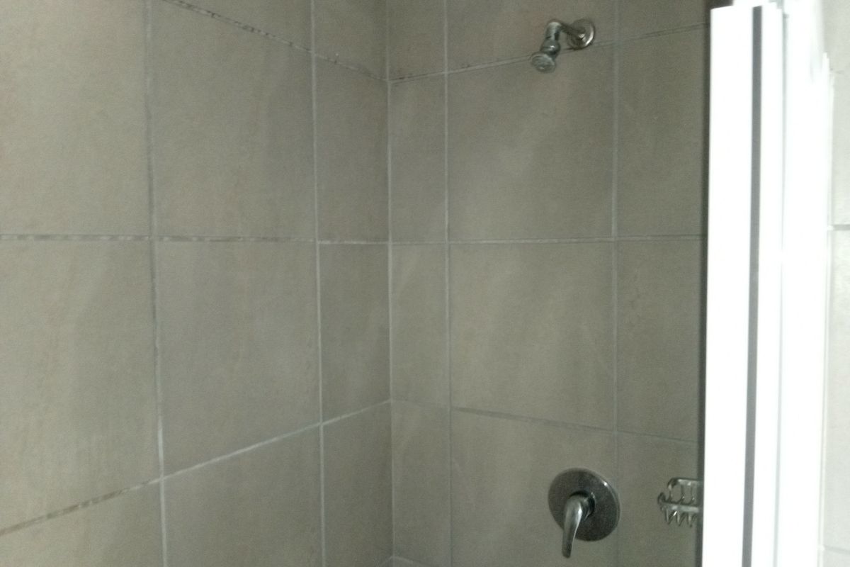 A functional shower enclosure featuring neutral wall tiles, a standard shower head, and a built-in soap dish.