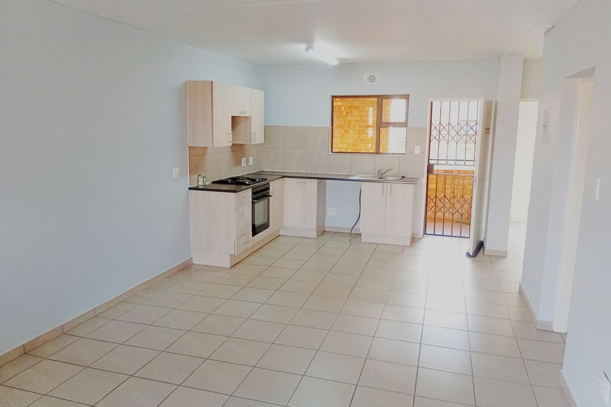 An open-plan kitchen and living area featuring light-toned cabinetry, tiled flooring, and direct access to an outdoor space through a security gate.