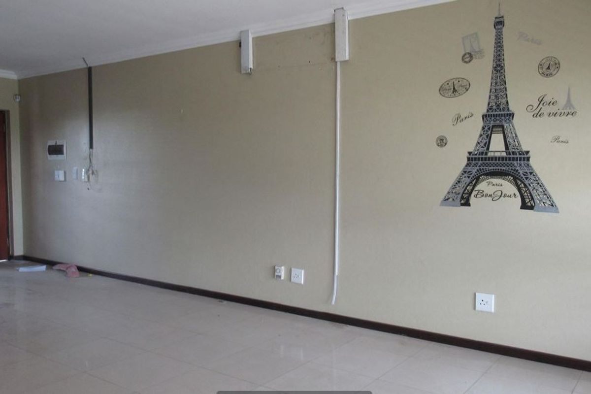 An empty living room featuring tiled flooring, coving, and exposed electrical wiring on the wall, offering a blank canvas for renovation and interior design.