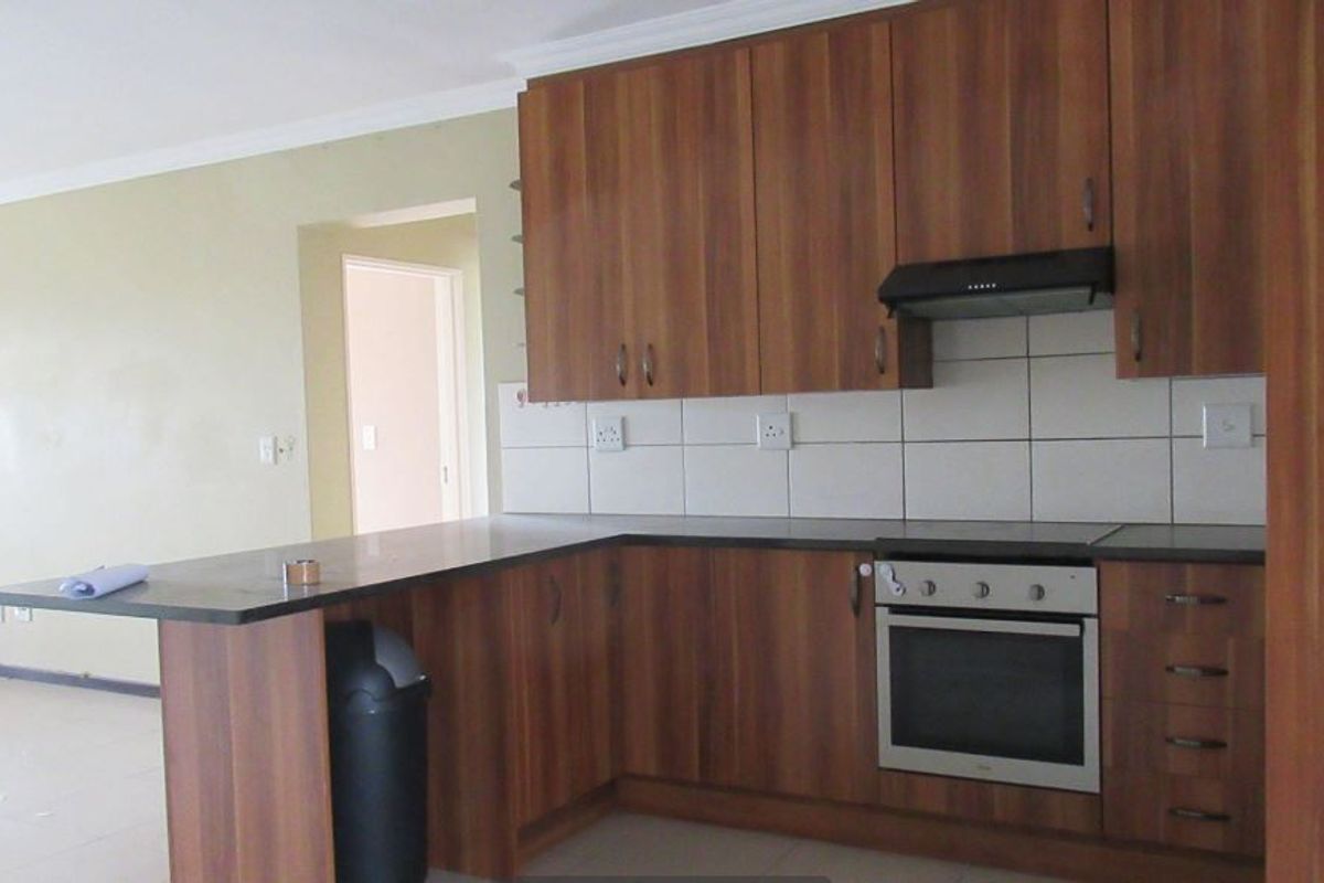A functional kitchen featuring wood-look laminate cabinetry, a built-in oven with extractor fan, tiled backsplash, and a convenient breakfast bar counter.