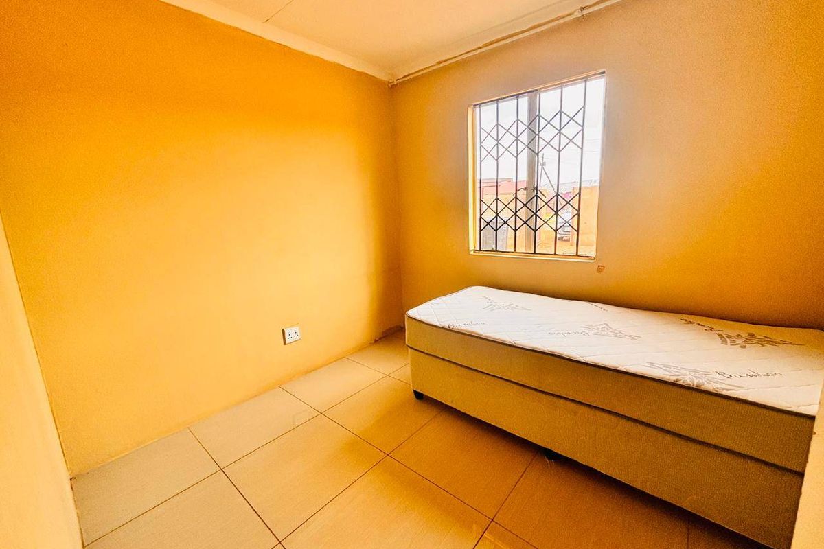 A simple bedroom featuring tiled flooring and a window fitted with security bars.