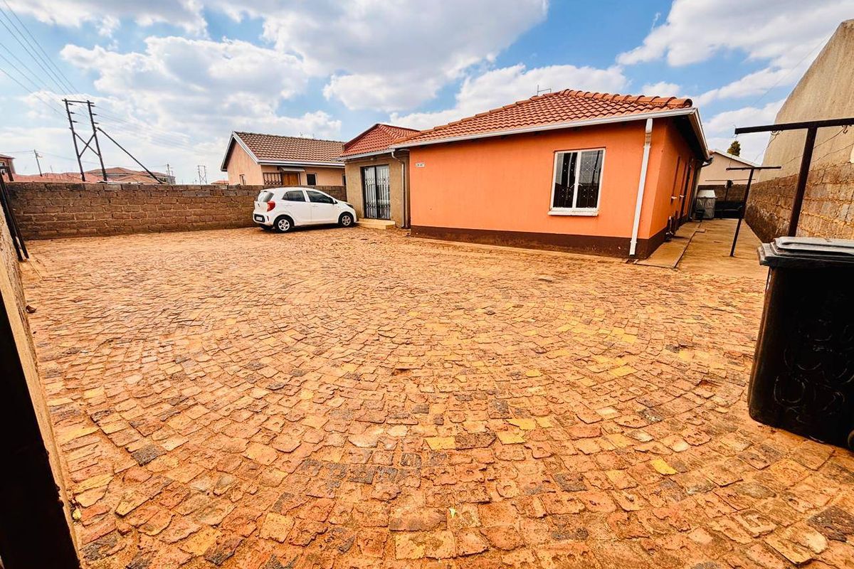 Spacious rear yard featuring extensive cobblestone paving, enclosed by a perimeter wall, providing ample outdoor space and parking area.