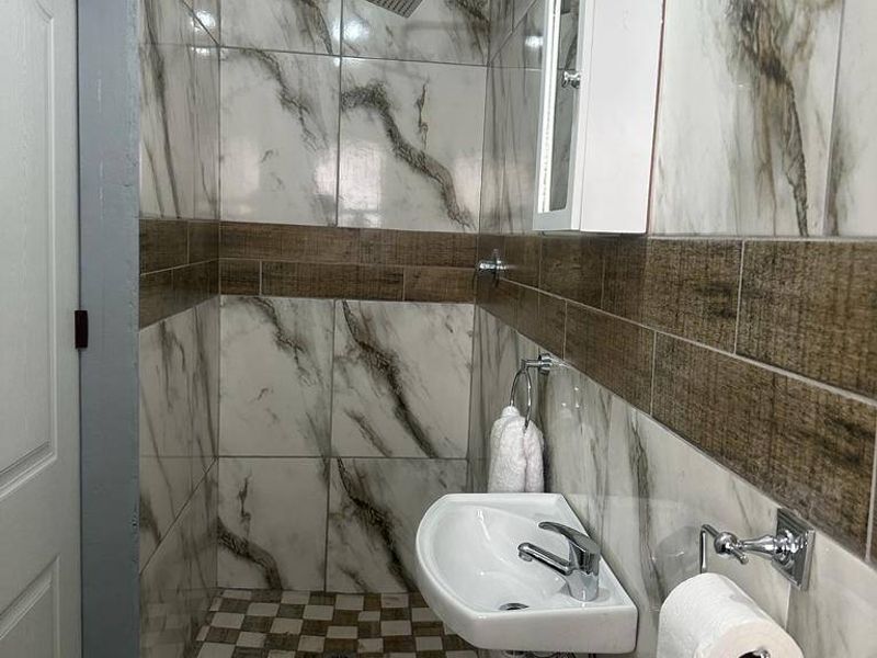 Compact bathroom featuring marble-look wall tiles, a walk-in shower area, and a wall-mounted basin with exposed plumbing.