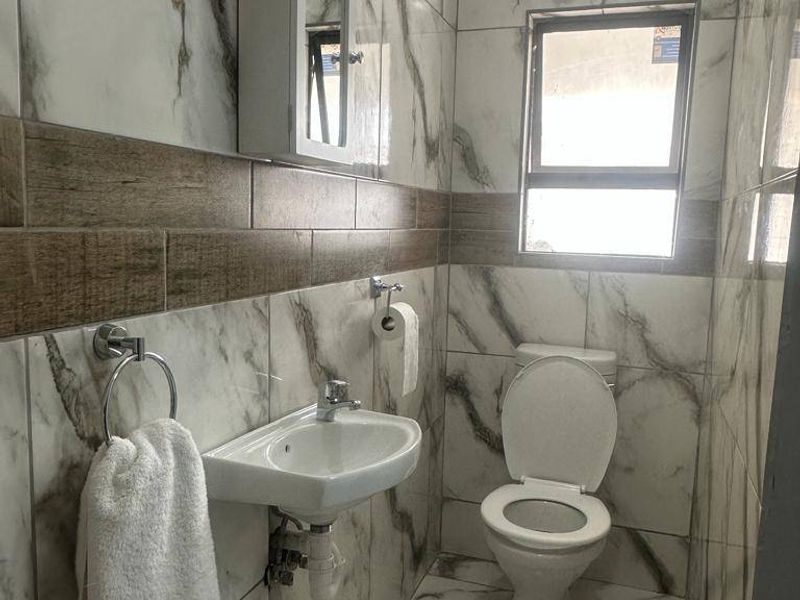 A modern, compact bathroom featuring marble-effect wall tiles, wood-look accent tiling, a wall-mounted basin, and a toilet.