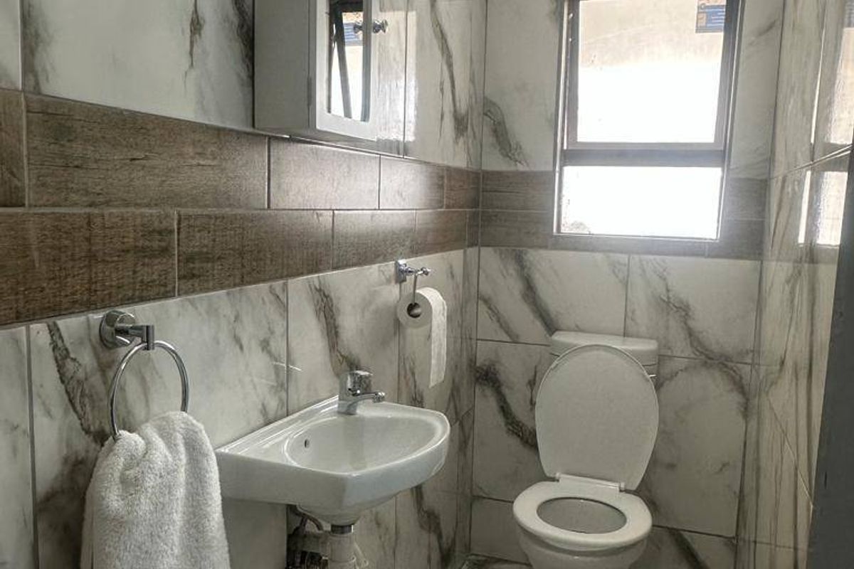 A modern, compact bathroom featuring marble-effect wall tiles, wood-look accent tiling, a wall-mounted basin, and a toilet.