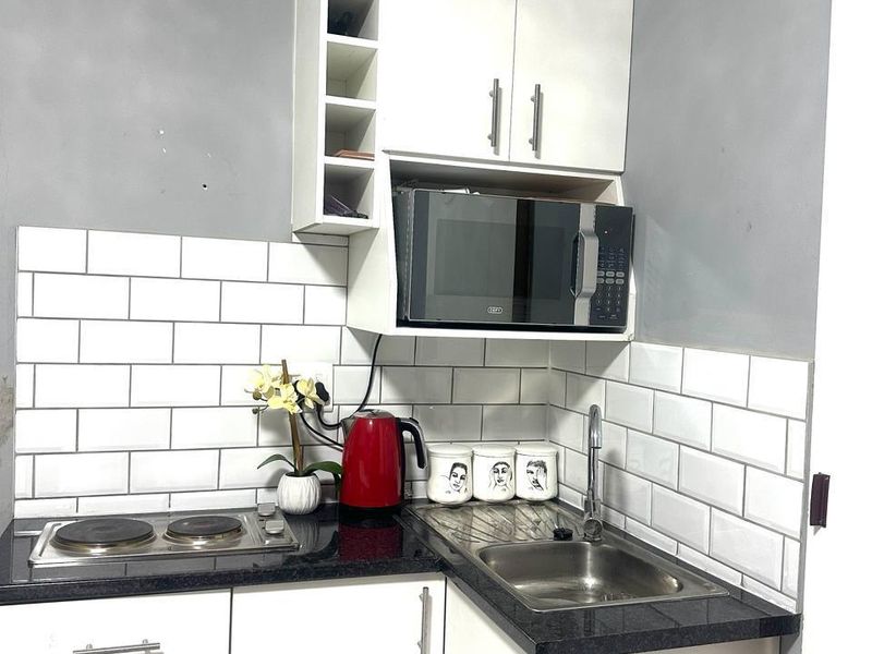Compact kitchen featuring white cabinetry, subway tile backsplash, black granite countertops, built-in microwave, and an electric hob.