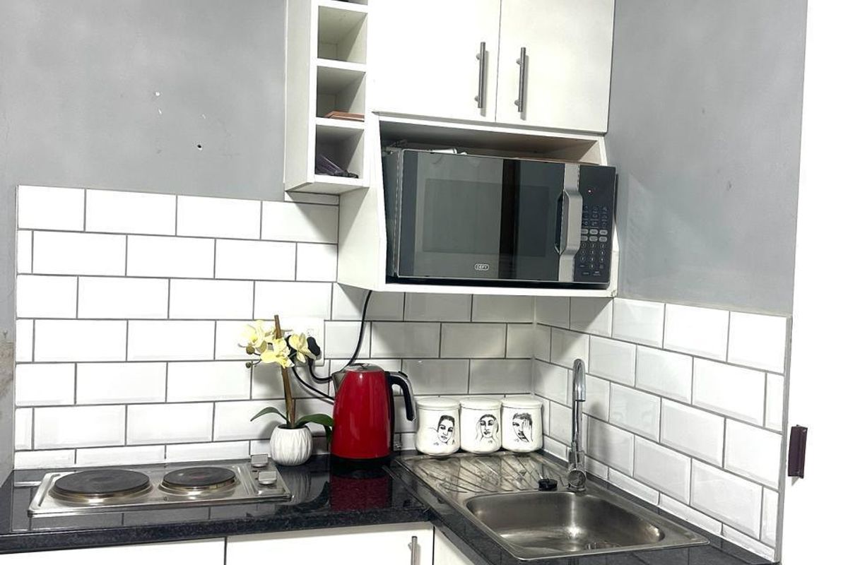 Compact kitchen featuring white cabinetry, subway tile backsplash, black granite countertops, built-in microwave, and an electric hob.