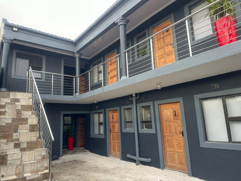 Exterior view of a multi-unit residential building featuring a concrete courtyard, tiled staircase, and stainless steel balustrades leading to upper-level access.