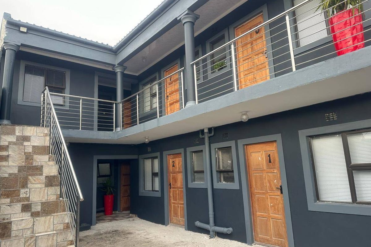 Exterior view of a multi-unit residential building featuring a concrete courtyard, tiled staircase, and stainless steel balustrades leading to upper-level access.