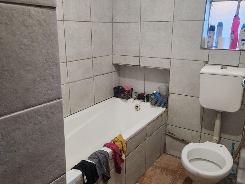 A functional bathroom featuring a bathtub, toilet, and tiled finishes. The space shows signs of wear and would benefit from modernization.