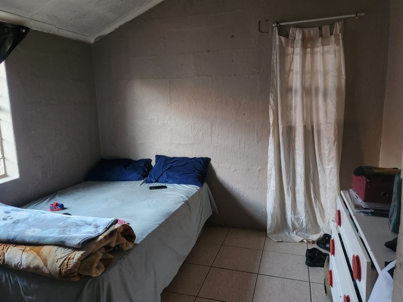 A bedroom featuring tiled flooring, exposed blockwork walls, and a sloped ceiling, offering a basic space ready for cosmetic updates and finishing.