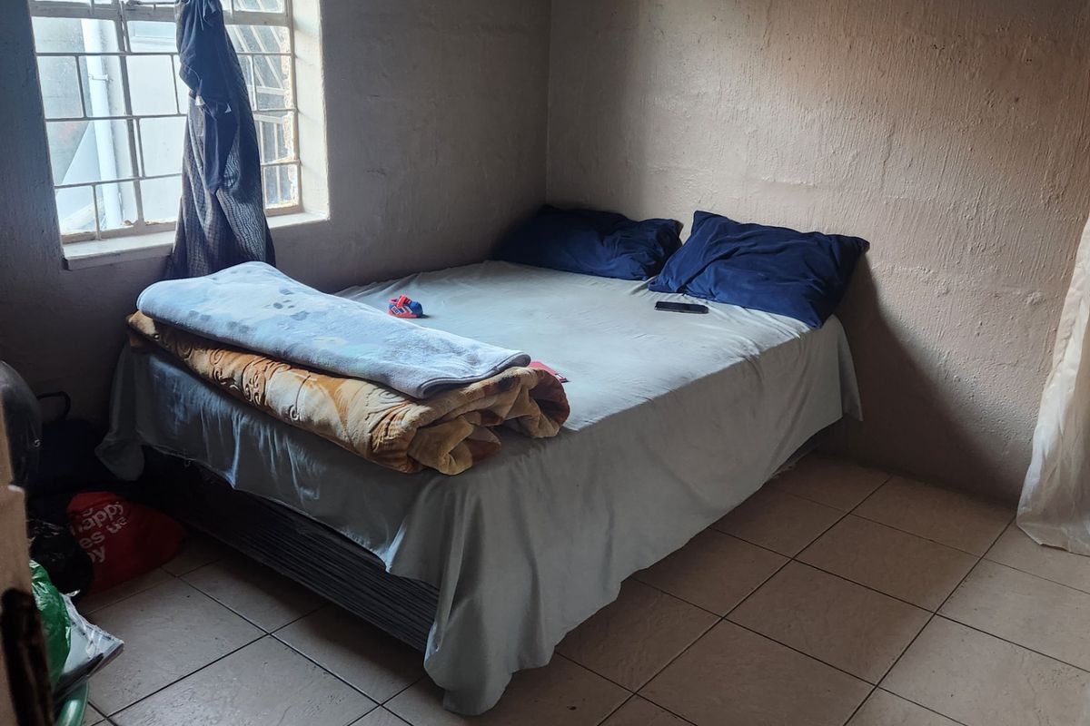 A compact bedroom featuring tiled flooring and a window with security bars, requiring cosmetic updates to the wall finishes.