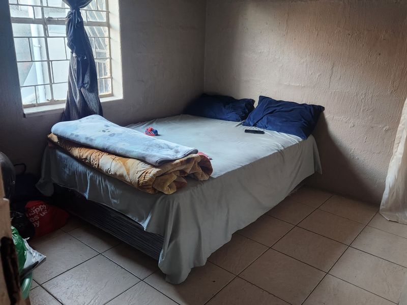 A compact bedroom featuring tiled flooring and a window with security bars, requiring cosmetic updates to the wall finishes.