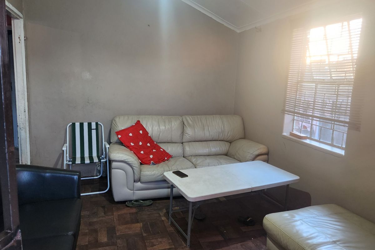 A living room featuring parquet flooring, a vaulted ceiling, and venetian blinds, currently requiring cosmetic updates to the wall finishes and flooring.