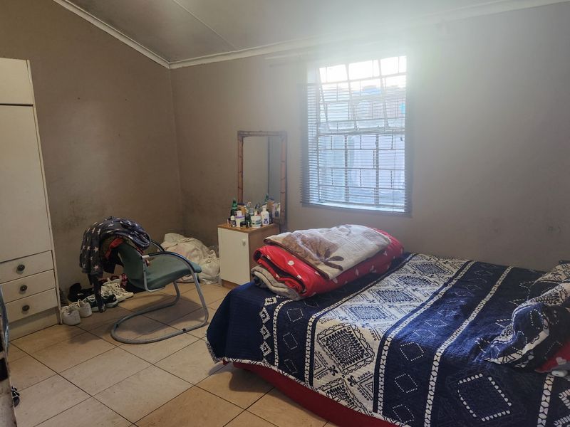 A bedroom featuring tiled flooring, a built-in wardrobe, and a window with blinds. The room requires cosmetic updates to the wall finishes.