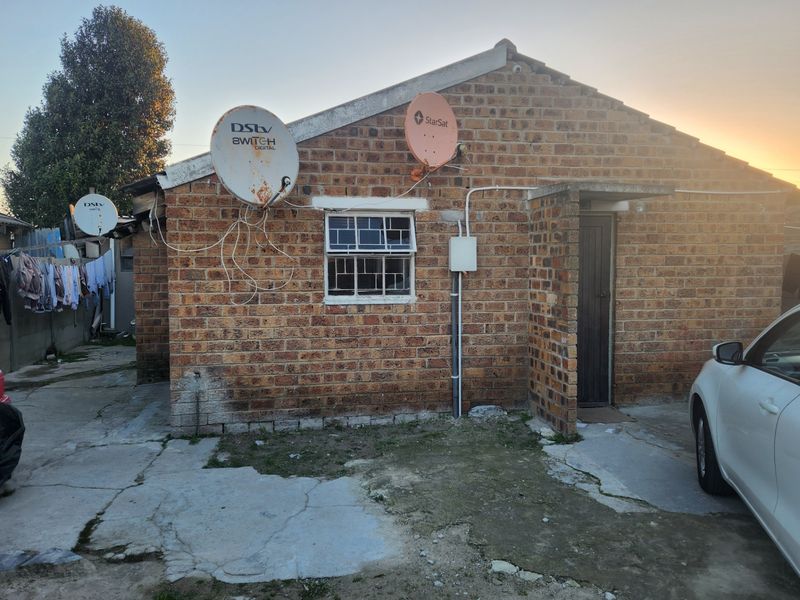 Front exterior view of a face brick house featuring multiple satellite dishes, a security door, and a concrete driveway in need of maintenance.