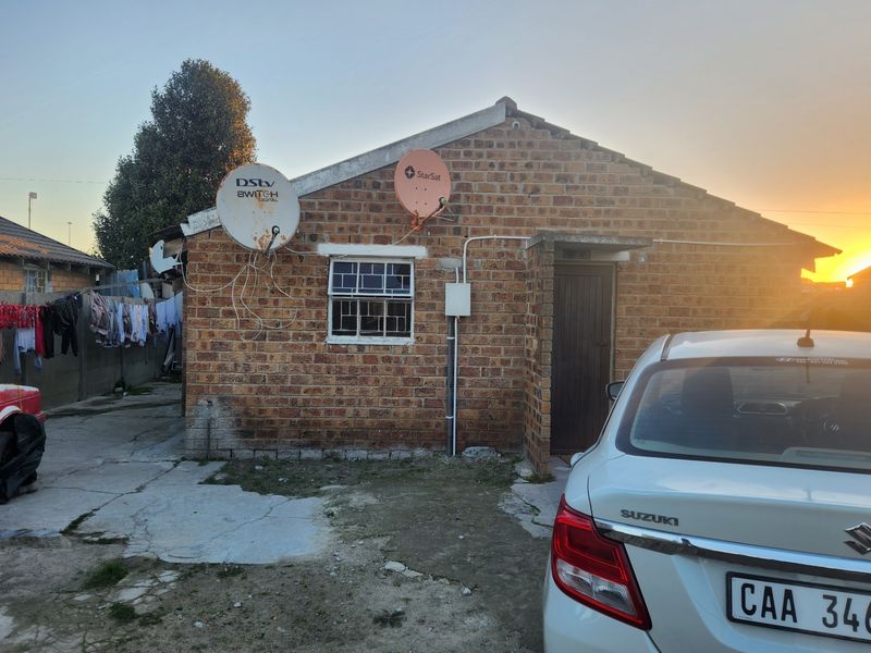 Rear view of a face brick house featuring satellite dishes, security window bars, and a concrete driveway area.