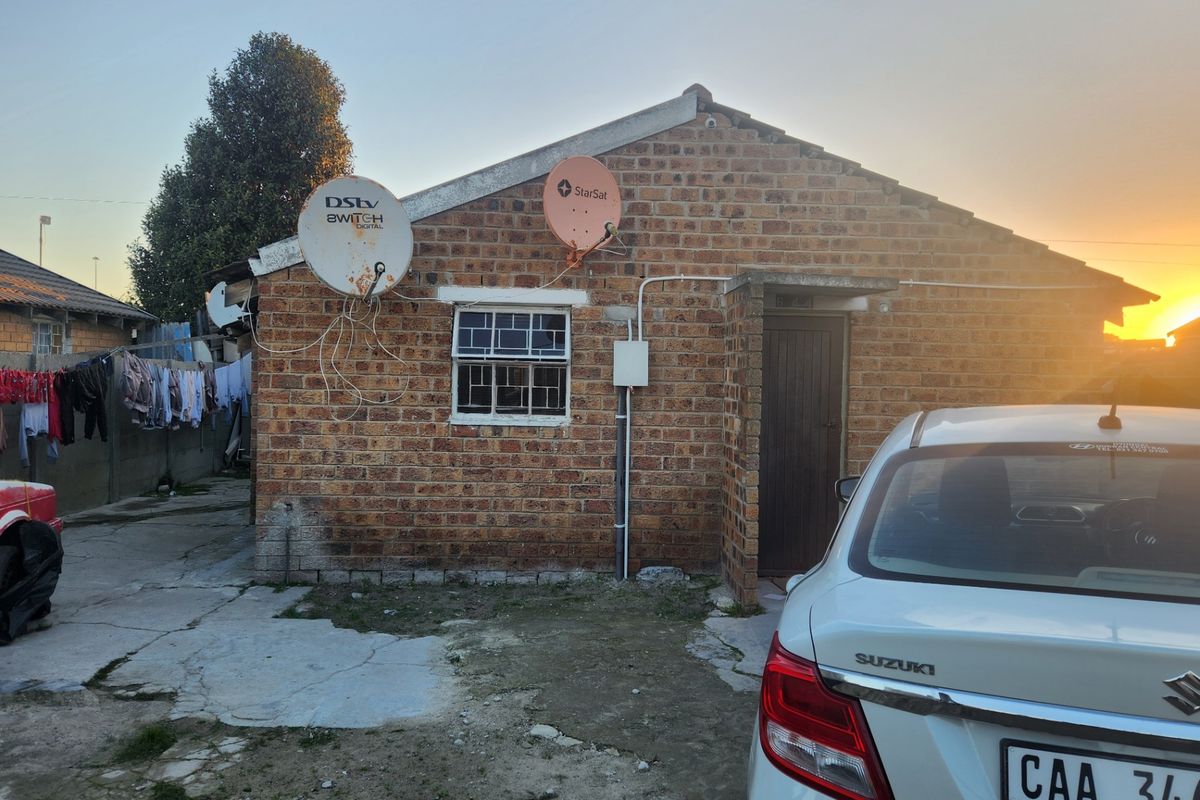 Rear view of a face brick house featuring satellite dishes, security window bars, and a concrete driveway area.