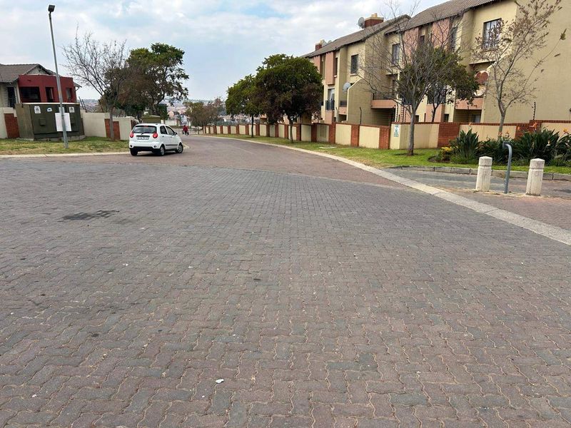 A view of the paved street and surrounding residential apartment complex with boundary walls and security fencing.