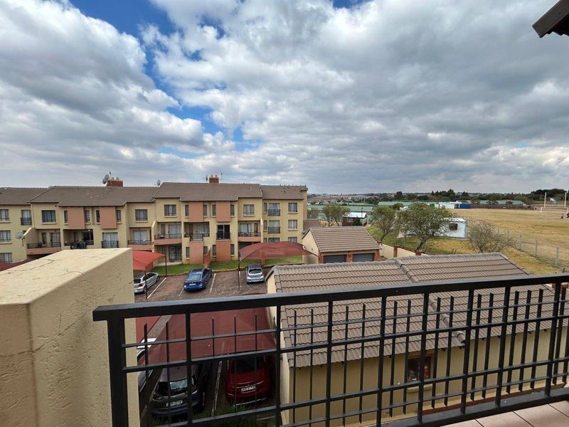 Elevated view from a balcony overlooking the apartment complex parking area, carports, and surrounding landscape.