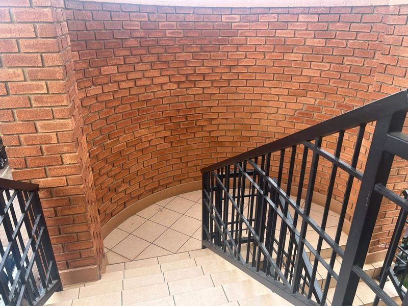 A curved staircase featuring exposed brick walls, tiled steps, and a black metal balustrade.