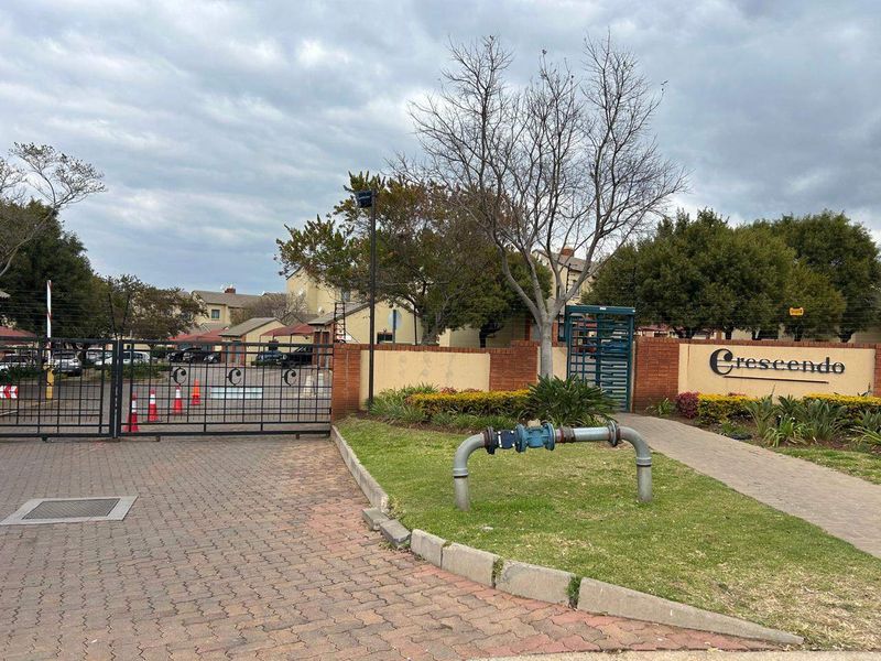 Entrance view of the Crescendo apartment complex featuring a secure gated access point, brick boundary wall, and landscaped garden area.