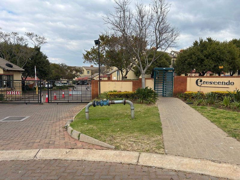 The entrance to the Crescendo apartment complex featuring secure gated access, brick boundary walls, and paved driveway infrastructure.