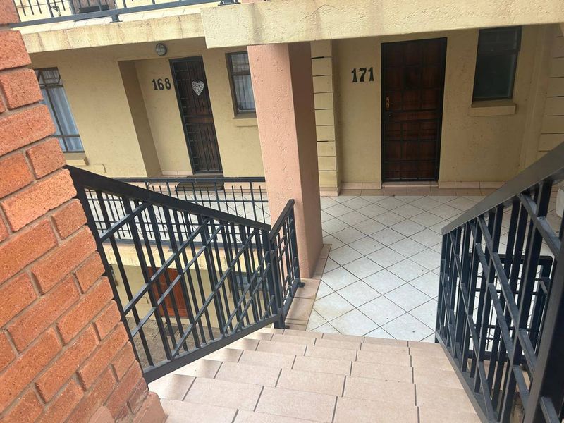 Exterior view of an apartment complex walkway featuring tiled stairs, metal balustrades, and individual unit entrances with security gates.