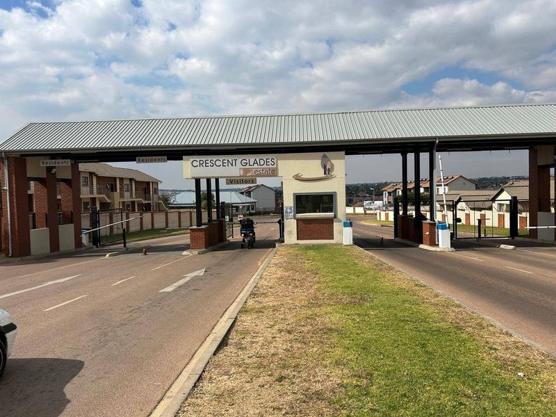 The main entrance and security gatehouse of Crescent Glades estate, featuring controlled access boom gates and a paved driveway.