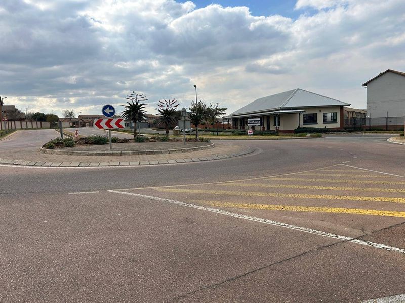 A view of the residential estate entrance featuring a paved roundabout and the community clubhouse building.