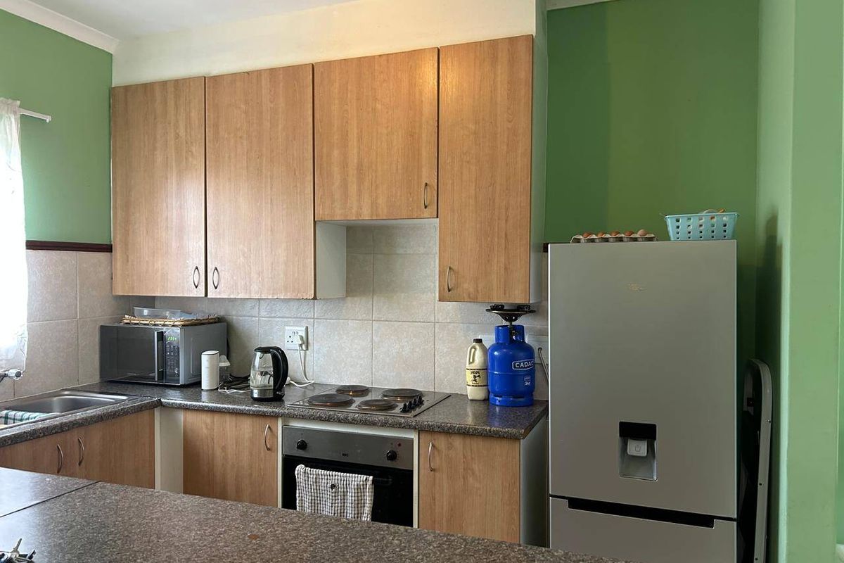 A functional kitchen featuring wood-look cabinetry, stone-effect countertops, a built-in oven, and a tiled backsplash, offering a practical layout for daily use.