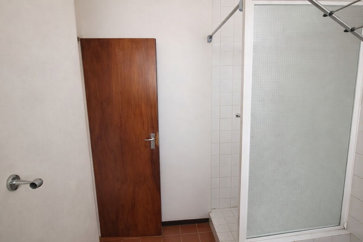 A functional bathroom featuring a tiled shower enclosure and a timber door, presenting a clean but dated aesthetic ready for modernization.